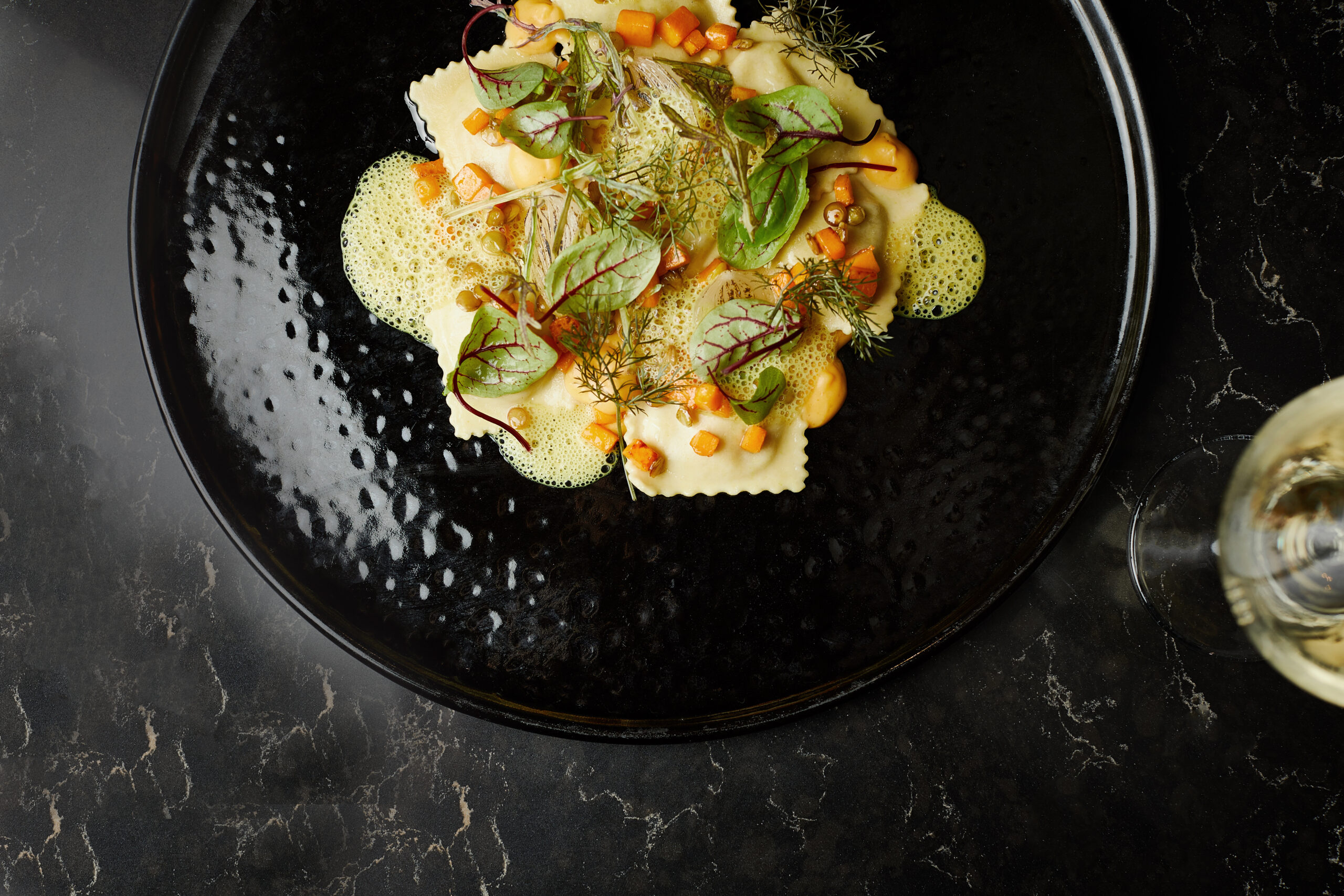 Exquisite fine dining dish with artistic plating, foam garnish & microgreens on black plate. Gourmet cuisine with sophisticated presentation.